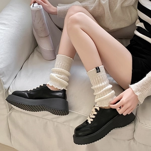 Detail of cream knit leg warmers with logo tag and black platform leather shoes