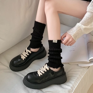 Japanese style black knit leg warmers paired with platform loafers on soft background