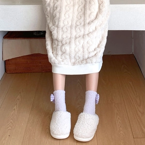 Detail of purple coral fleece socks with checkered bow and plush white slippers