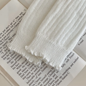 Macro shot of white knit leg warmer with ribbed texture and ruffled edge on a book
