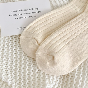 Detail der cremefarbenen Rippstrick-Wintersocken auf weicher Decke mit Kunstkarte