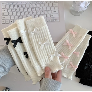 Détail de jambières en maille avec nœuds et bords ondulés en rose, blanc et noir