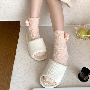 Pink coral fleece socks with plaid bows and white waffle slippers in a cozy home setting