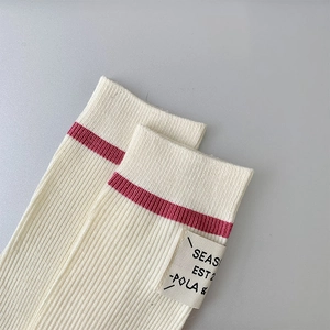 Close-up of ribbed knit wool socks in beige with a red stripe and minimalist fabric label
