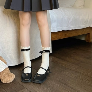 Detail of white ribbed crew socks with black velvet bow, pearl, and ruffles