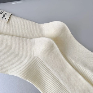 Detail of cream rib-knit wool socks featuring a minimalist textile label and heel stitching