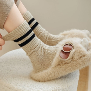 Detail of cable knit wool socks with black stripes paired with plush beige slippers