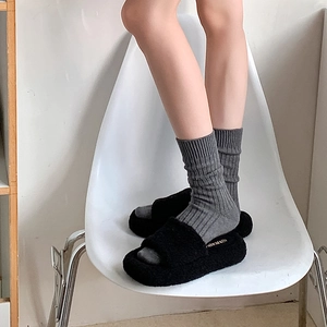 Detail von plüschigen schwarzen Plateauslippern mit grauen Rippsocken auf weißem Stuhl