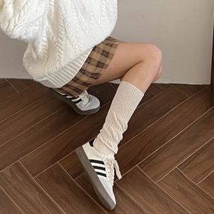 Detailed view of cream knit knee-high socks with cable pattern and sporty sneakers
