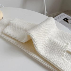 Close-up of white ribbed knit leg warmer on a minimalist desk with soft lighting