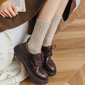 Detail of beige cable knit crew socks paired with vintage brown leather shoes
