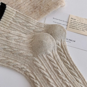 Detailed close-up of thick beige cable-knit wool socks featuring black contrast stripe