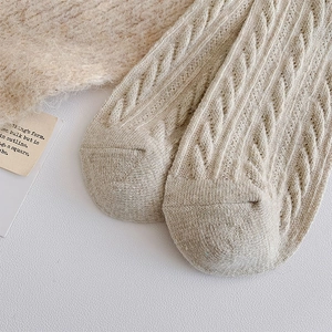 Detailed macro view of beige cable knit wool socks showing thick texture and stitching