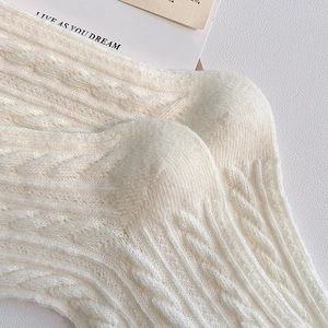 Macro shot of white cable knit crew socks showing thick cotton warmth and soft texture