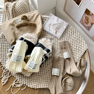 Detail of ribbed knit crew socks with fabric tag and plush slides in earth tones