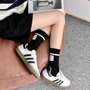 Close-up of black wool crew socks with white stripes and woven label on leather stool