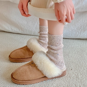 Close-up of thick thermal wool socks paired with suede fur-lined slippers in winter setting