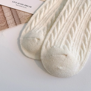 Close-up of cream white thick knit socks showing detailed cable patterns and warm texture