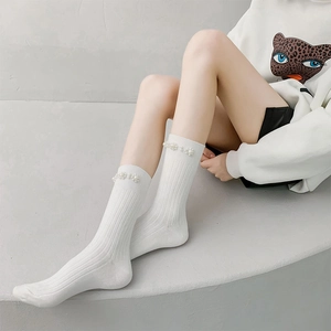 Detail view of white ribbed calf socks featuring elegant faux pearl embellishments at the cuff