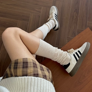 Detail shot of ivory knit calf socks paired with brown plaid skirt and striped sneakers