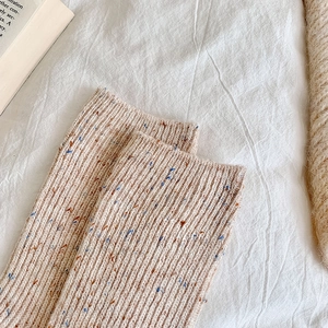 Close-up of thick beige wool socks with colorful flecks and vertical ribbed knit texture