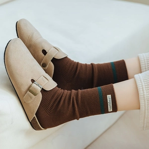 Dettaglio di sabot in camoscio beige abbinati a calze marroni a righe con etichetta verde