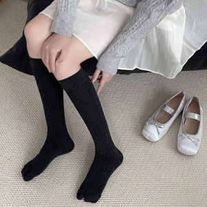 Detail von schwarzen Tabi-Socken mit Rippmuster, silbernen Schuhen und weißem Rock