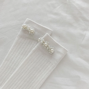 Close-up of white ribbed knit socks featuring elegant pearl flower ornaments at the cuff