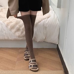 Detail of dark brown ribbed wool over-knee socks paired with buckled winter sandals