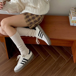 Detail of retro sneakers with three stripes paired with cozy knitted knee-high socks