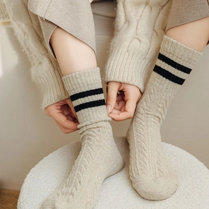 Close-up of beige wool socks featuring cable knit texture and black double stripes