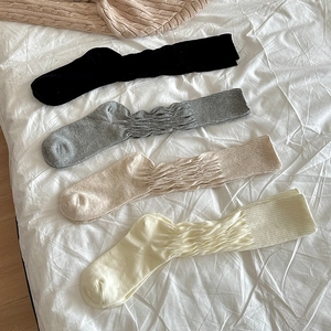 Detail of four colors of knitted slouch socks in black, gray, beige, and cream cotton