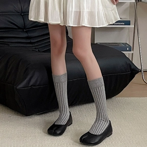Detail of grey striped tabi socks paired with black split-toe flats and white pleated skirt