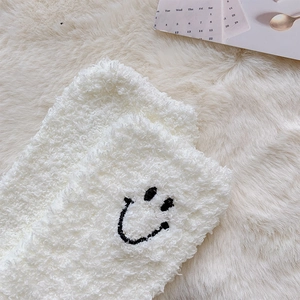 Detailed macro view of white coral fleece socks featuring a cute embroidered smiley face design