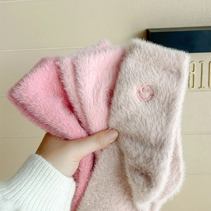 Dettaglio calzini di peluche rosa e beige con ricamo a forma di sorriso e tessuto caldo