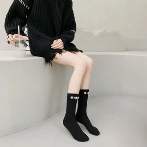 Detail of black mid-calf socks with ribbed knit texture and white pearl flower trim