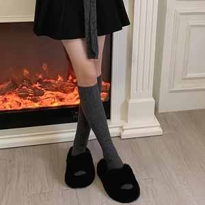Detail of gray knitted ribbed wool socks paired with warm black plush slippers at home