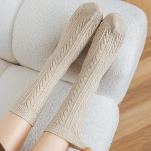 Close-up of beige cable knit warm socks with ribbed cuffs on a soft sofa