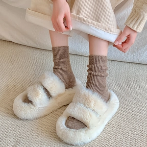 Close-up of cream white fuzzy slippers with double bands worn with warm ribbed brown socks