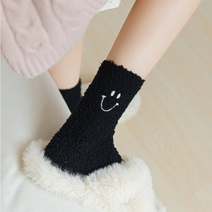 Detail of black coral fleece socks with white smiley face embroidery and plush texture