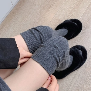 Detail of grey knitted over-knee wool socks with ribbed texture and fuzzy slippers