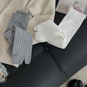 Close-up of ribbed white and striped grey tabi socks on a beige knit texture