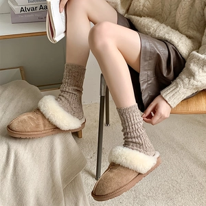 Close-up of brown suede slippers with thick white faux fur trim and wool knit socks