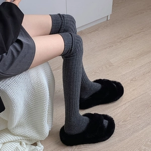 Close-up of thick knitted over-the-knee socks and plush slippers on a cozy wooden floor