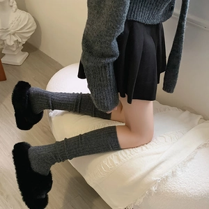 Detail of dark grey ribbed knit leg warmers paired with black fuzzy platform slippers
