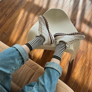 Dettaglio di calzini a righe e sneakers beige su uno sfondo di pavimento in legno