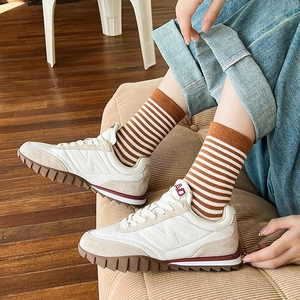 Sneaker retrò crema e kaki con suola in gomma ondulata rossa su pavimento in legno