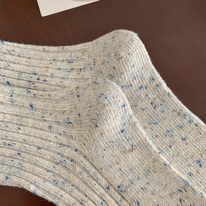 Macro detail of ribbed wool-blend knit socks with blue and brown speckles on wood background