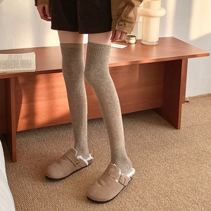 Close-up of khaki over-the-knee knit socks paired with plush-lined brown suede mules