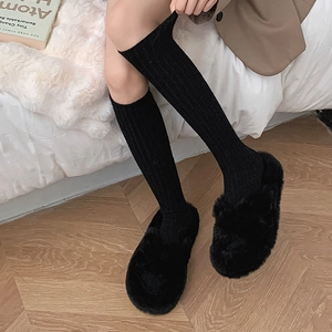 Close-up of black ribbed wool socks paired with plush slippers in a cozy home setting